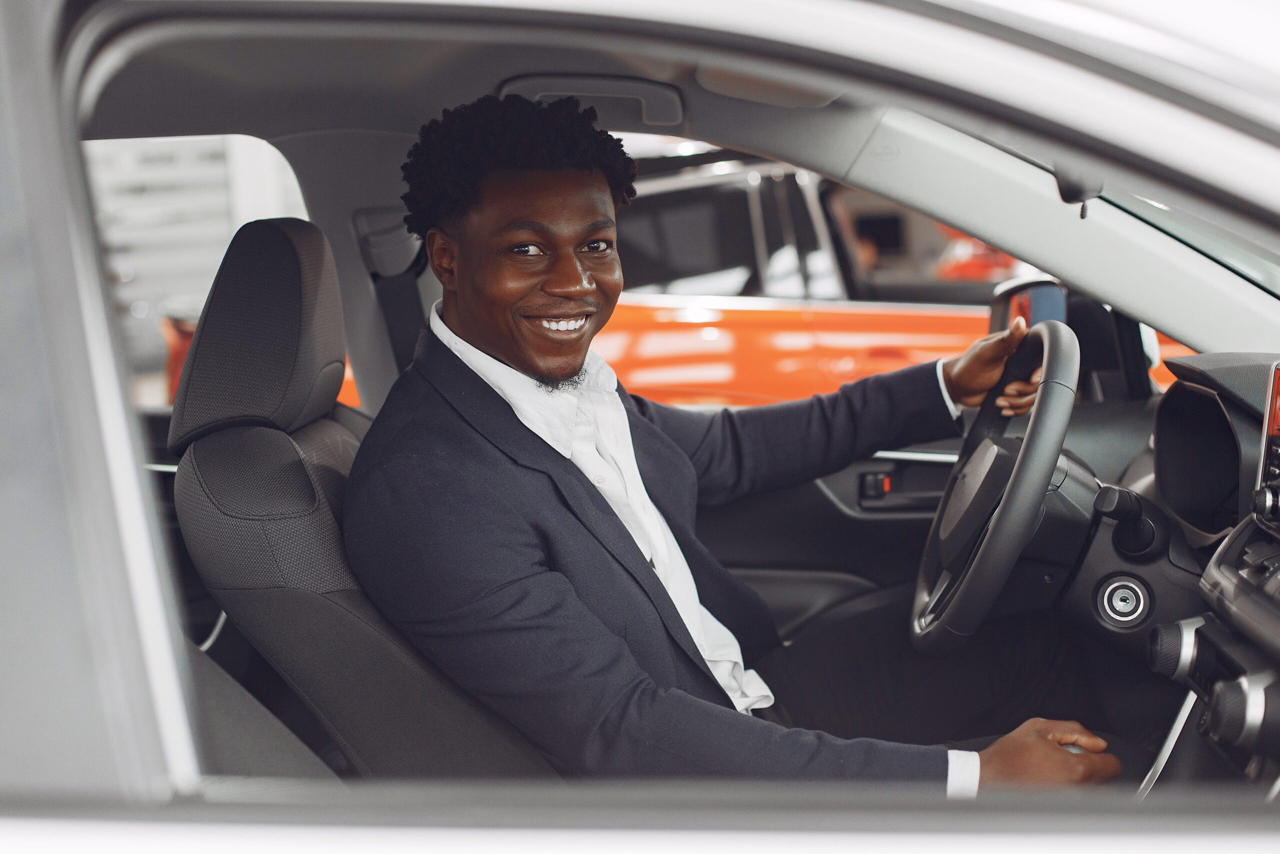 Man buying the car. Businessman in a car salon. Black male in a suit.