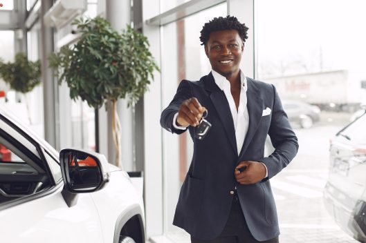 Man buying the car. Businessman in a car salon. Black male in a suit.